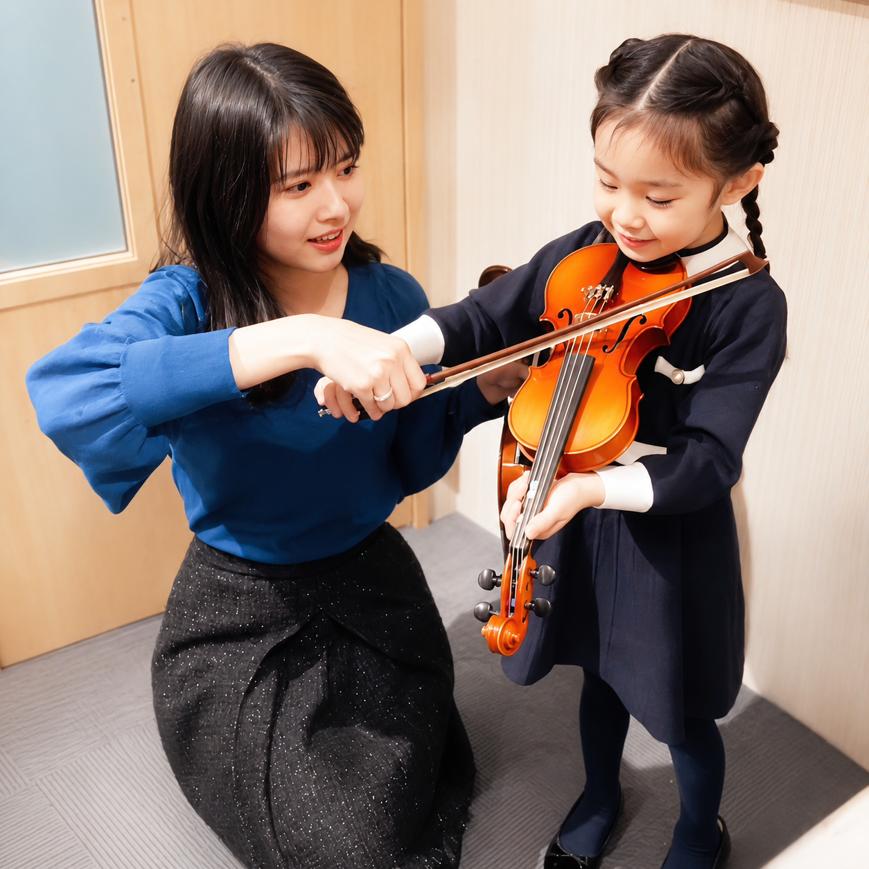 先生が子どものヴァイオリンの弓の使い方を教える様子